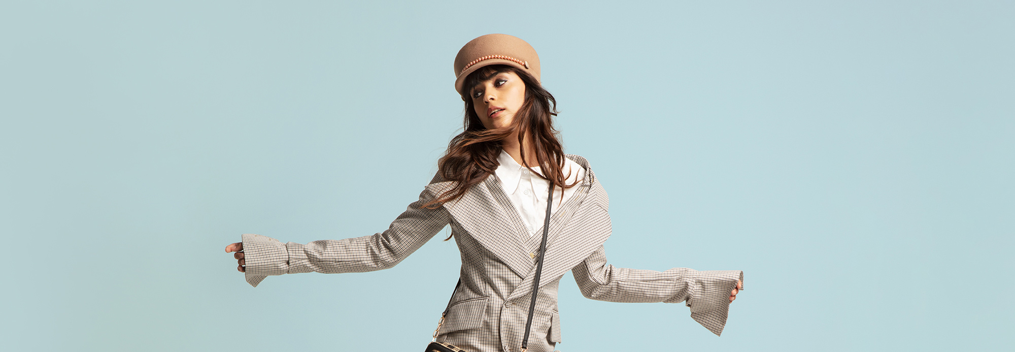 A woman wearing a conductor's cap and oversized blazer striking a pose