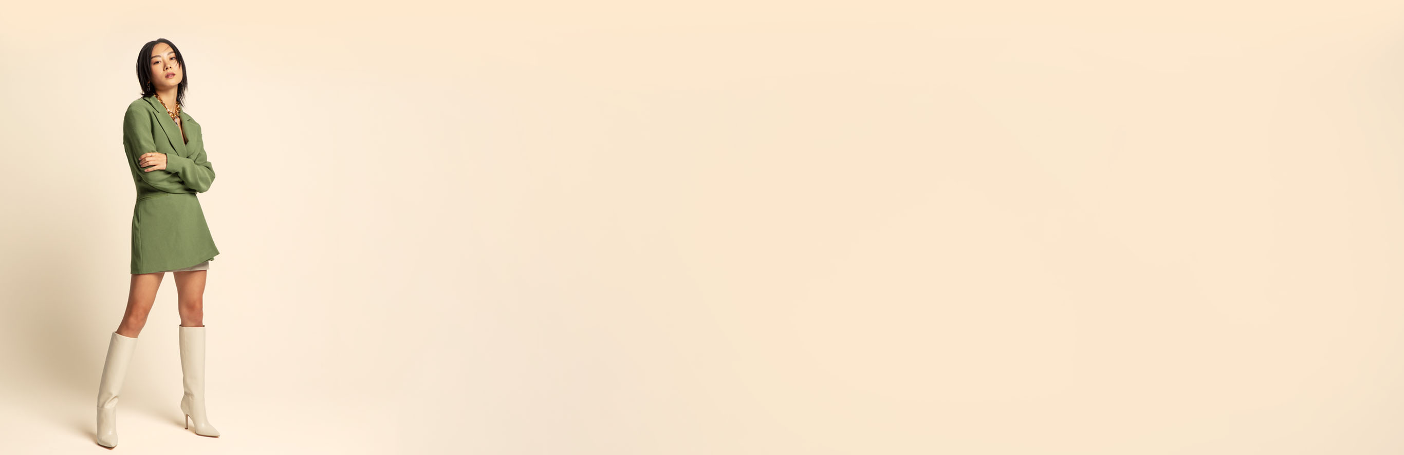 A woman wearing a green blazer-dress and knee-high cream-colored boots